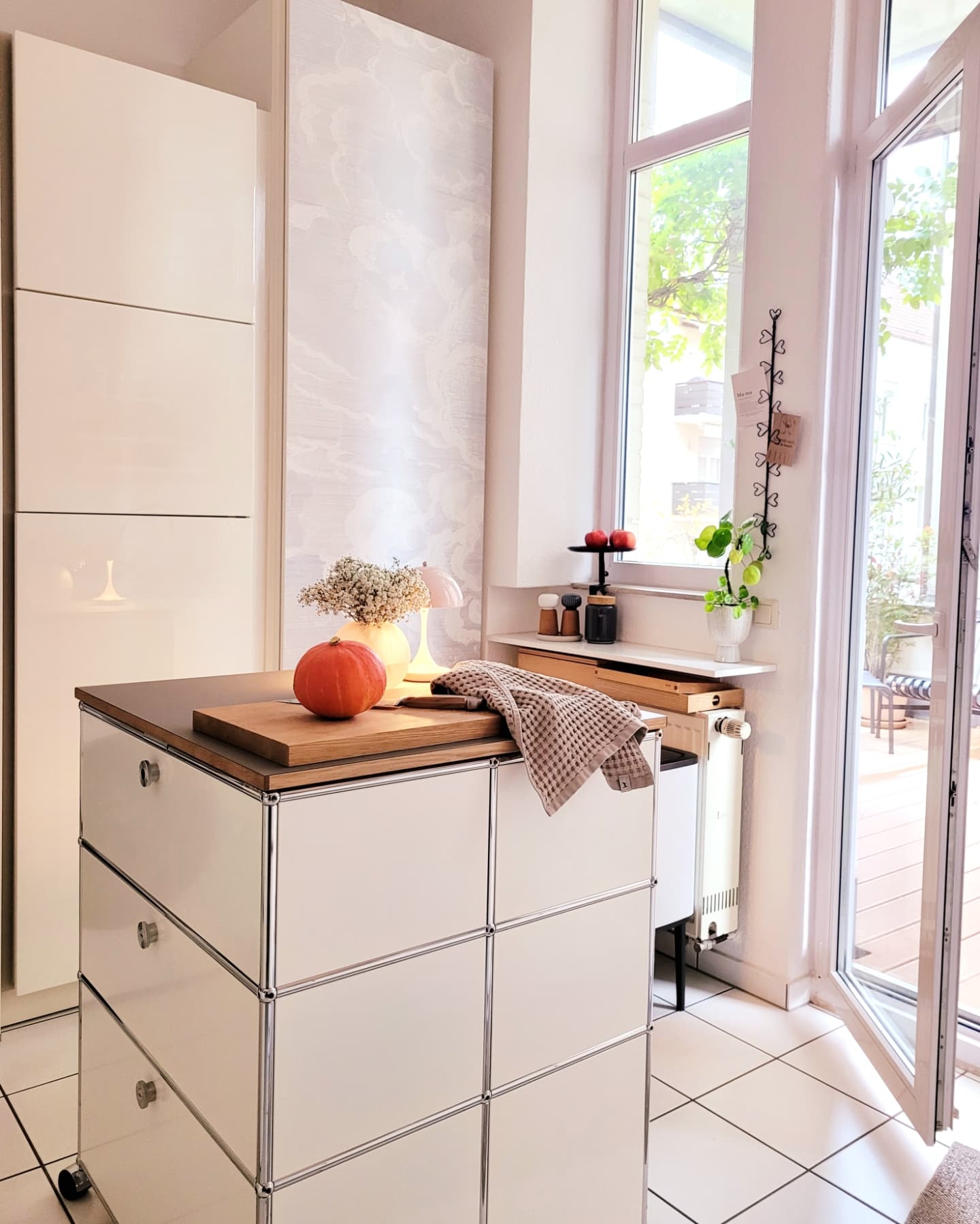 Lichte keuken met een wit USM Haller rolbaar eiland, houten blad en pompoen.