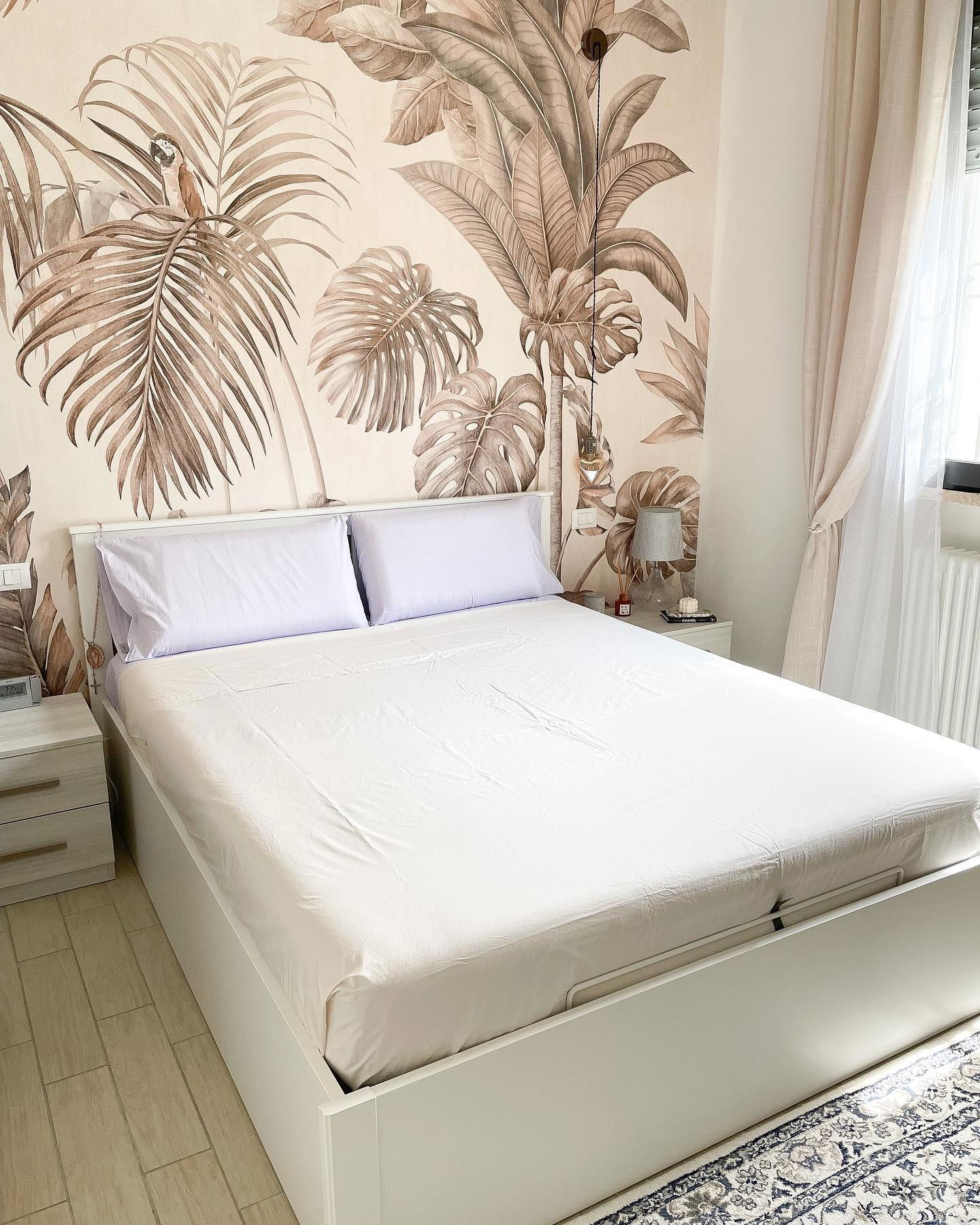 Bedroom with white bed, purple pillows, and tropical wallpaper.