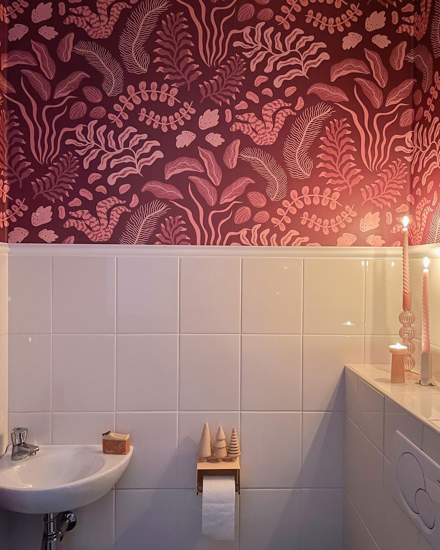 Small bathroom with floral wallpaper, white tile, sink, and lit candles.