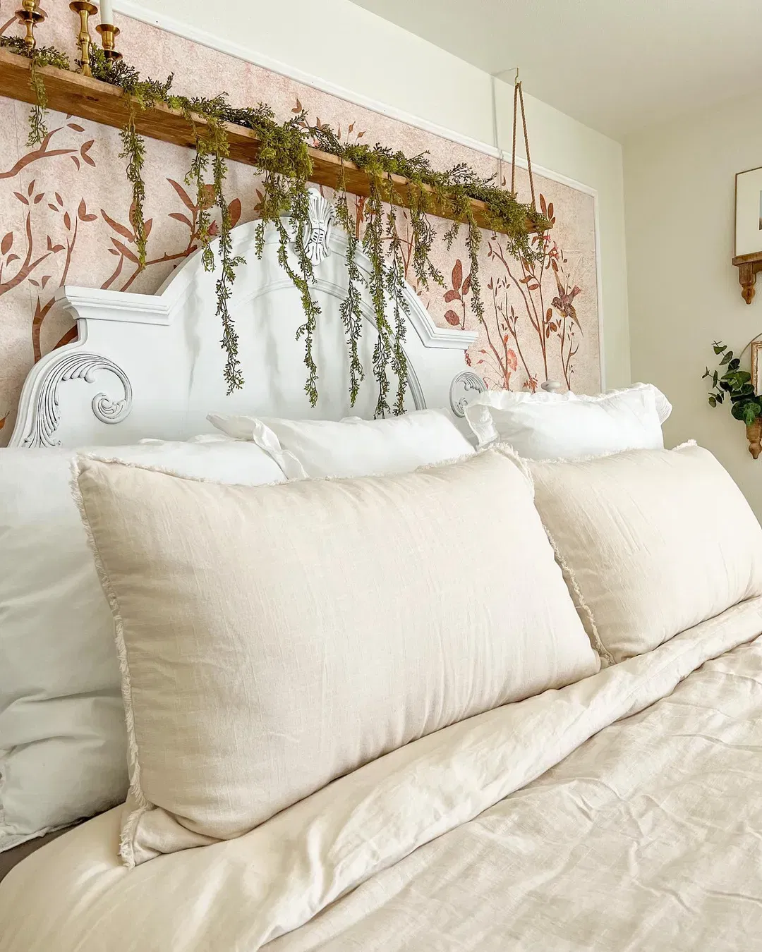 Bedroom with white headboard, floral wallpaper, and neutral bedding. Green garland hangs above the bed.
