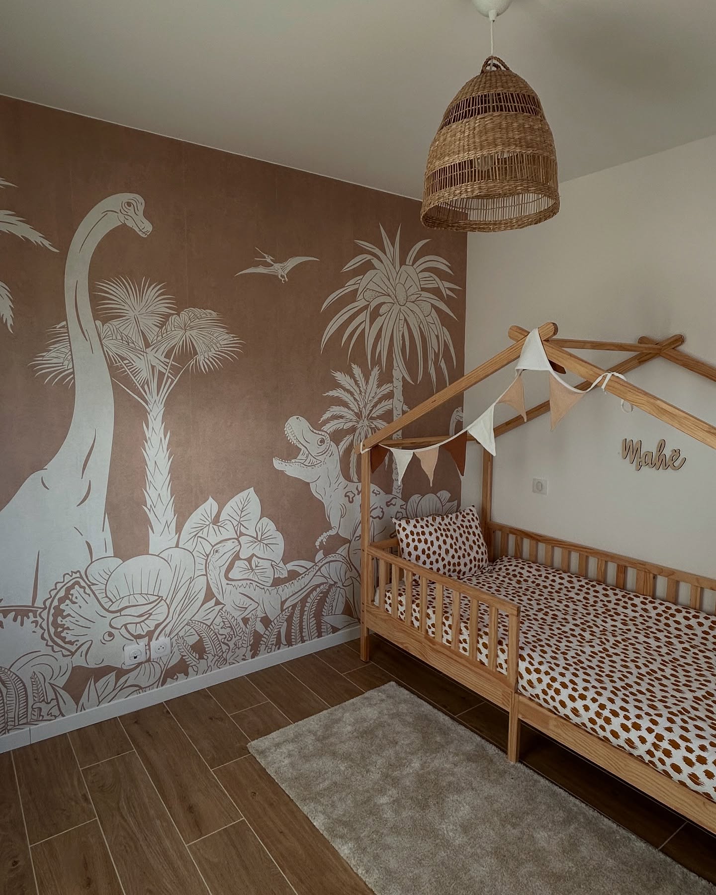 Chambre d'enfant avec une peinture murale de dinosaures, un cadre de lit en bois et une suspension tissée.