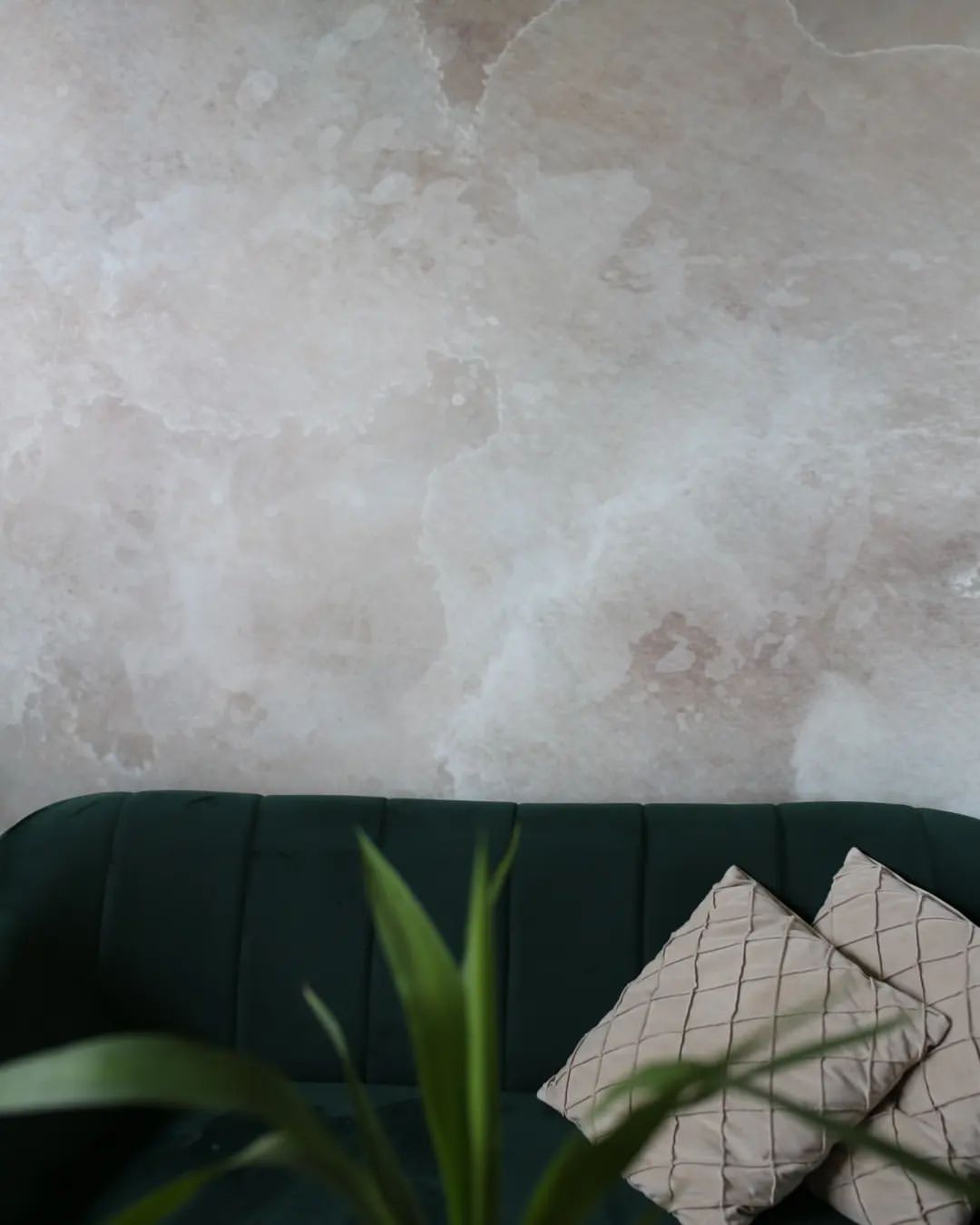 Interior con sofá de terciopelo verde, almohadas estampadas y pared texturizada.