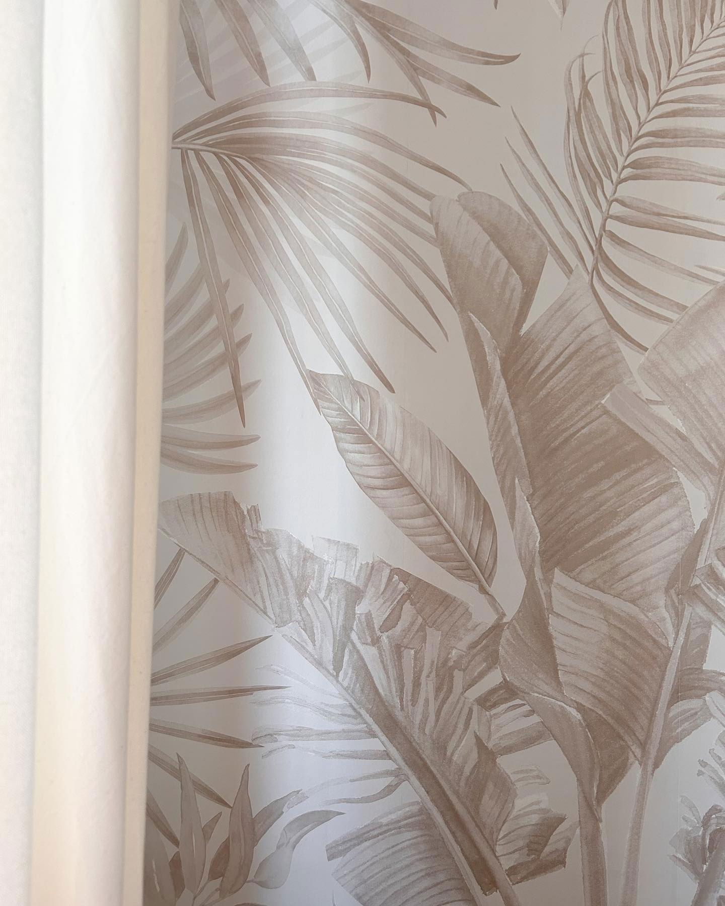 Close-up of beige tropical leaf wallpaper with white curtain.