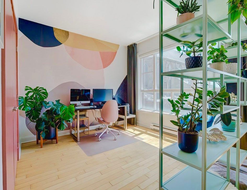 Bright home office with geometric wall art, plants, and light blue shelving.