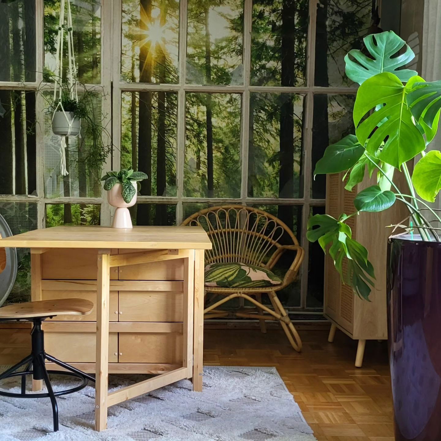 Interior with light wood desk, rattan chair, and forest window mural.