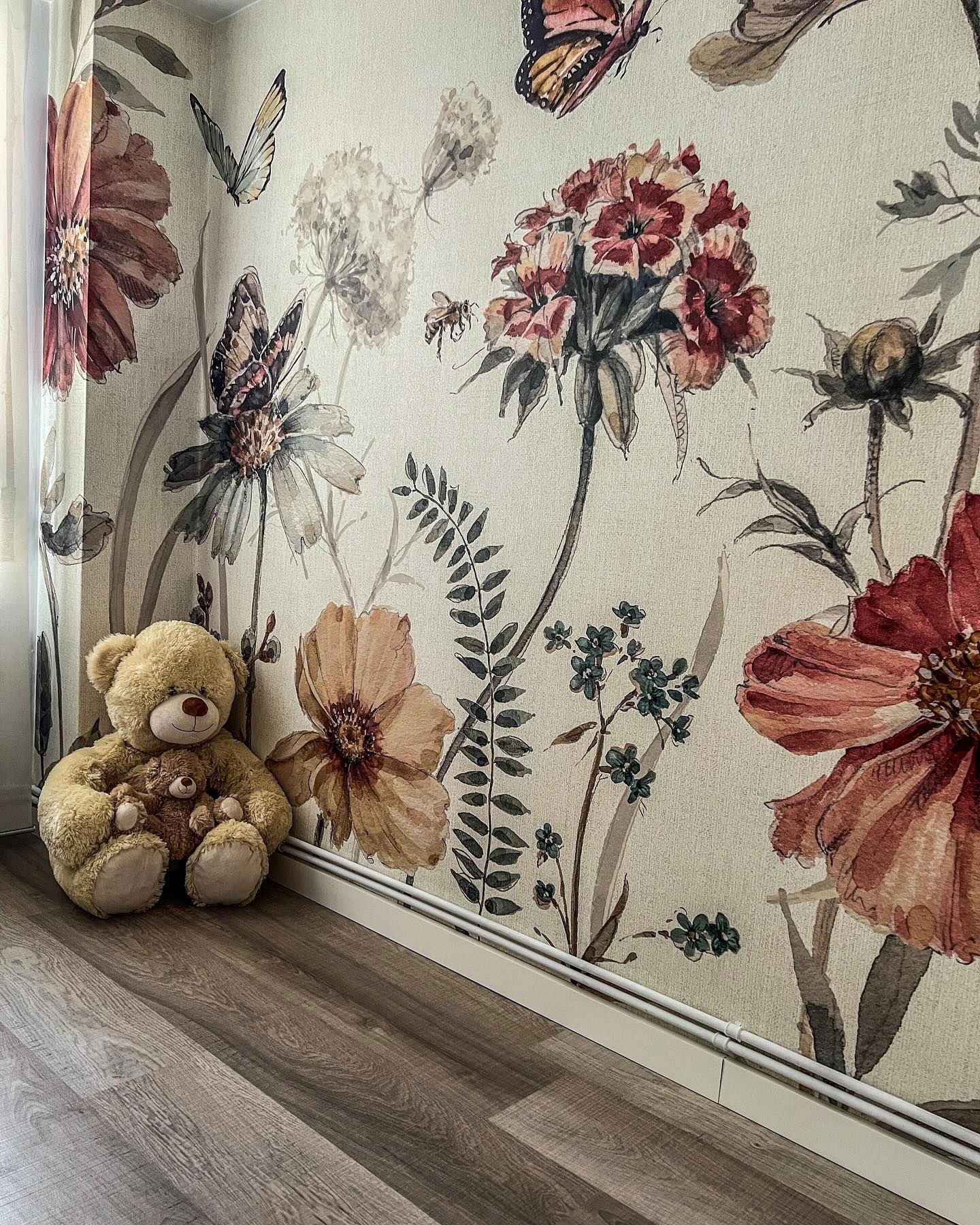 Teddybär mit Babybär sitzt vor Blumentapete auf Holzboden.