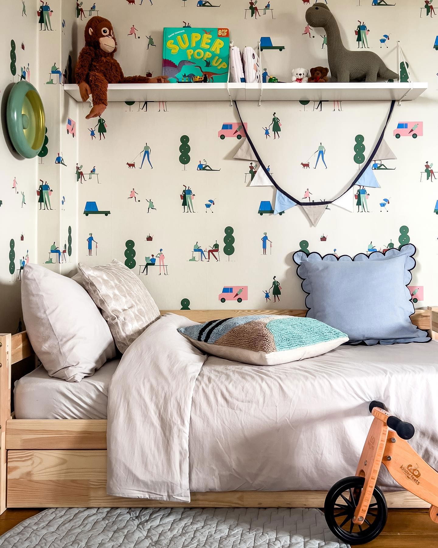 Child's bedroom with wooden bed, patterned wallpaper, and toys on a shelf.