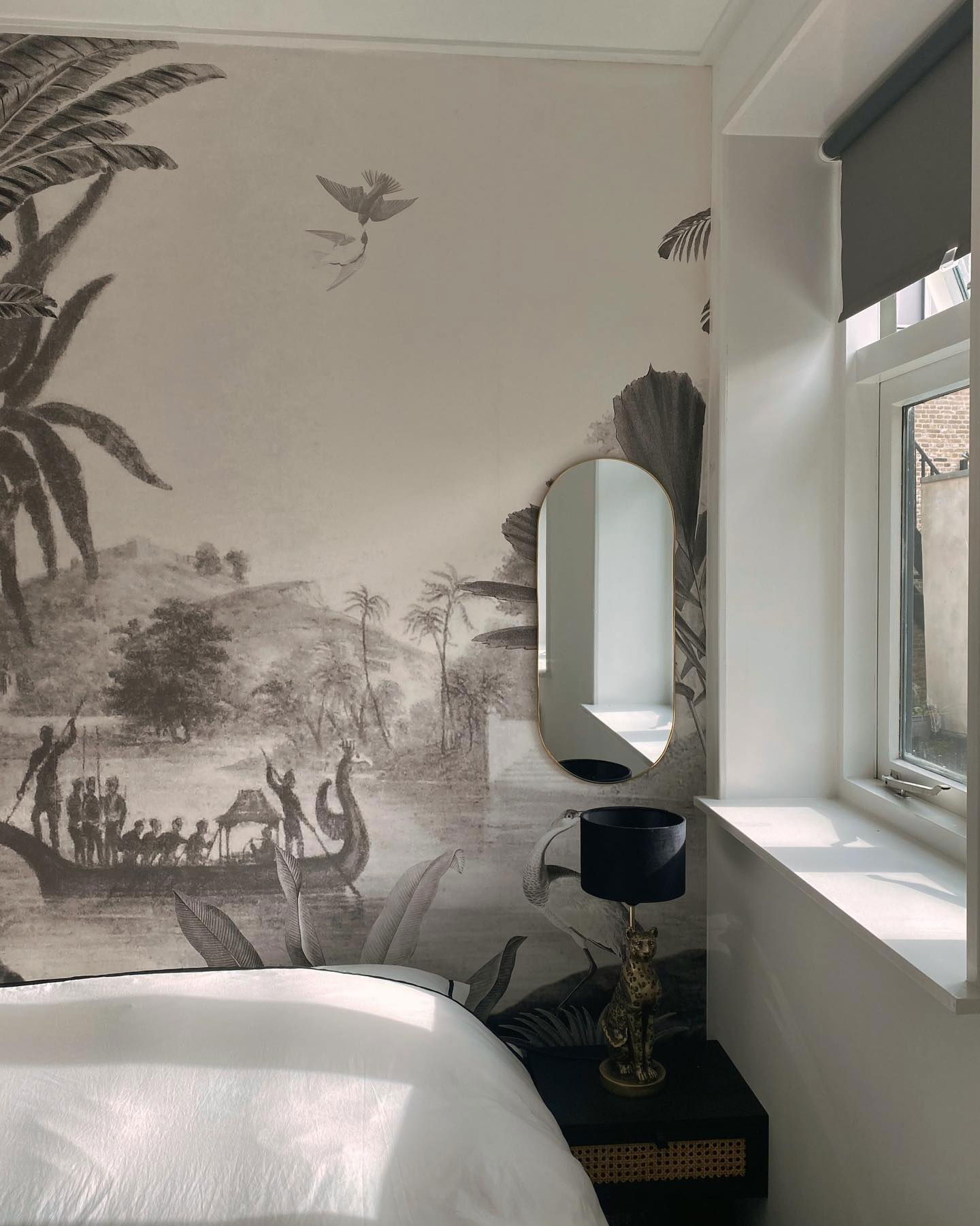 Bedroom with tropical mural, gold mirror, and black lamp with leopard base on a black nightstand.