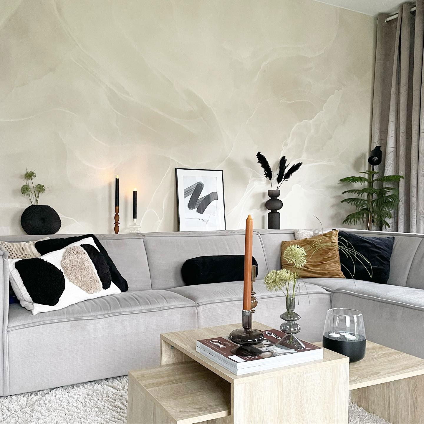 Soggiorno con divano componibile grigio, cuscini decorativi e tavolini da caffè ad incastro in legno chiaro su un tappeto bianco a pelo lungo.