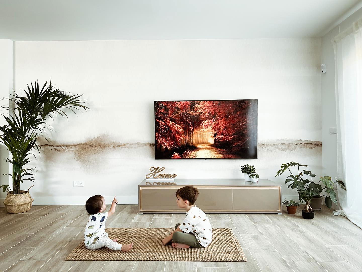 Living room scene with two children on a rug, TV, plants, and modern decor.