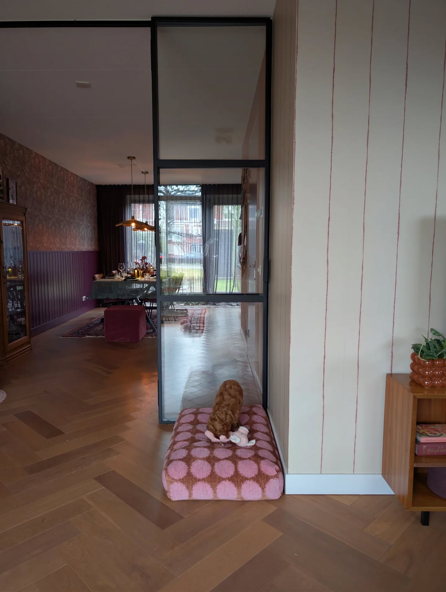 A fluffy brown dog rests on a pink patterned cushion in a modern room.