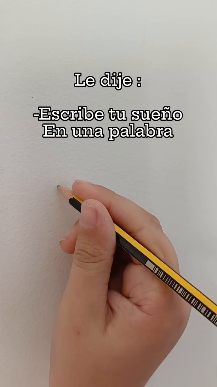 Hand holding a yellow pencil to write "Escribe tu sueño En una palabra" on a white wall.