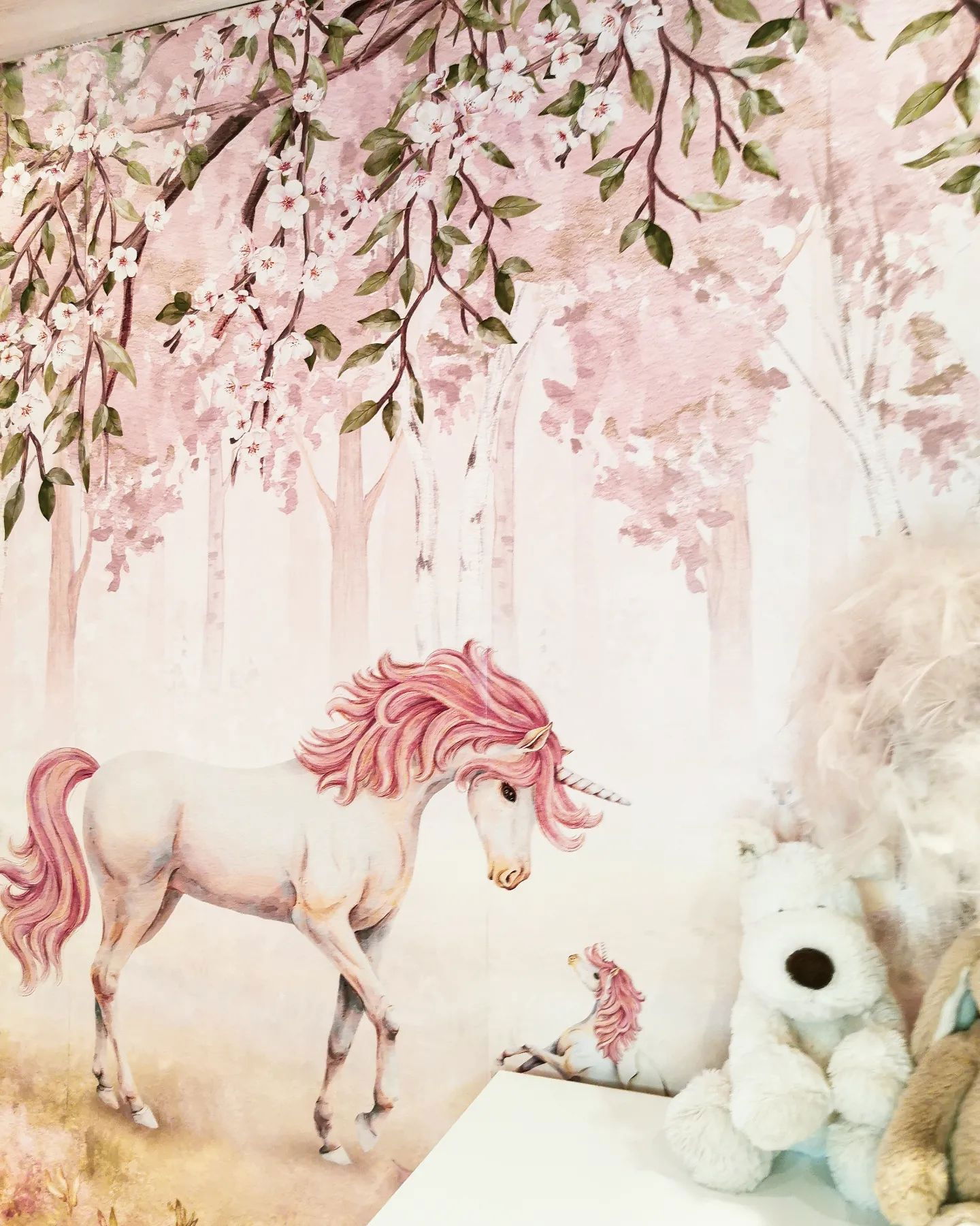 Unicorn-tapet i akvarellstil med rosa skog och gosedjur på en hylla.