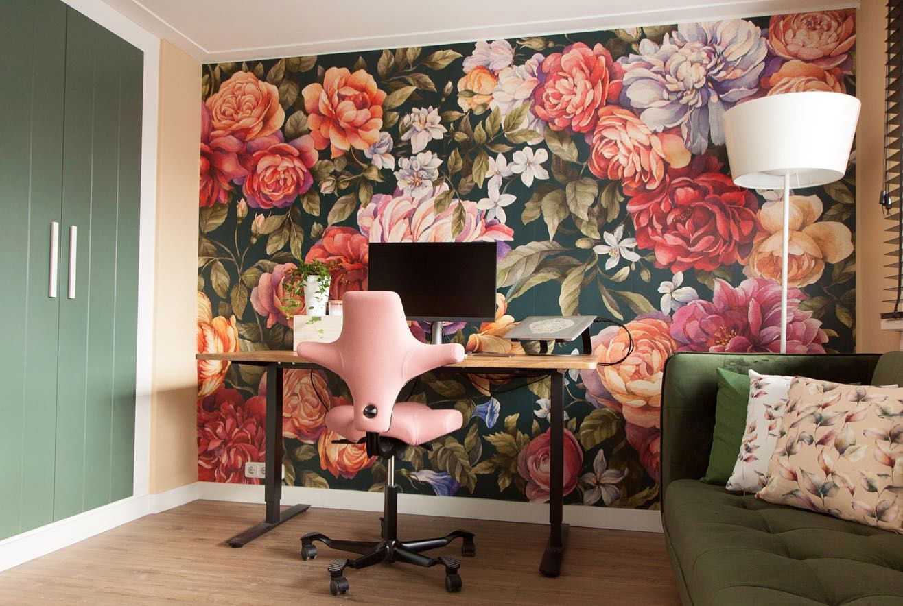 Interieur met bloemenbehang, bureau, roze stoel, groene bank en groene kast.