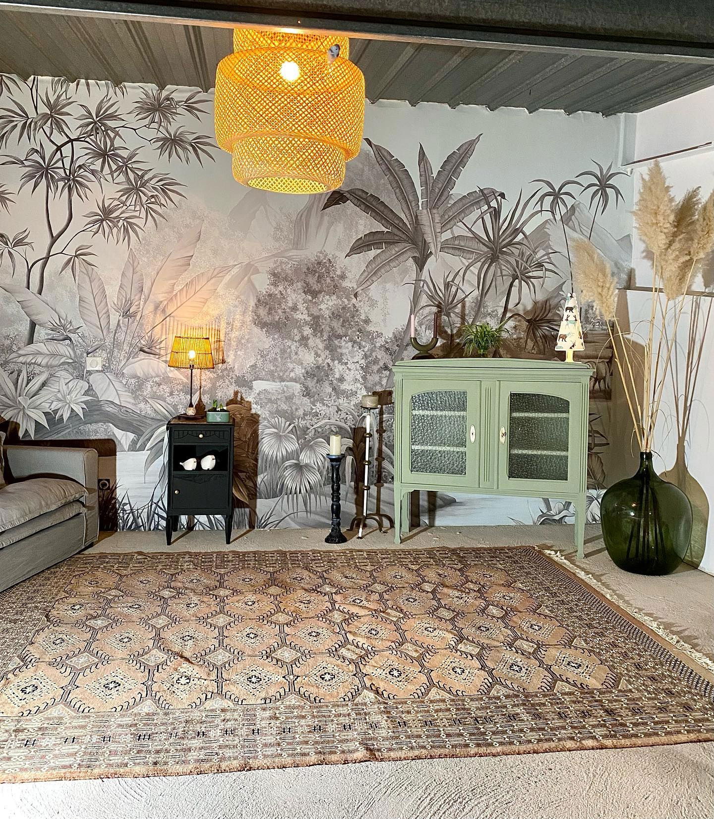 Eklektisches Wohnzimmer mit Dschungel-Wandgemälde, gemustertem Teppich und Vintage-Möbeln.