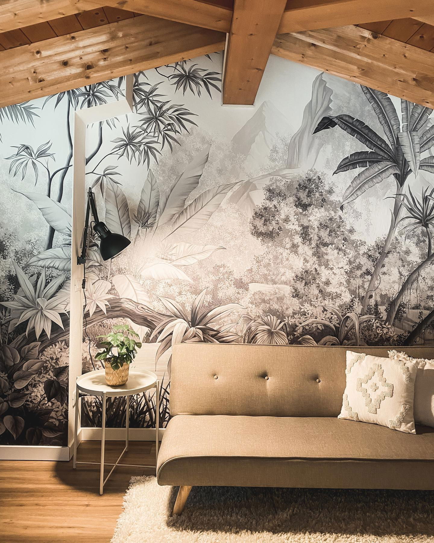 Stue med tropisk veggmaleri, beige sofa og hvitt sidebord med plante.