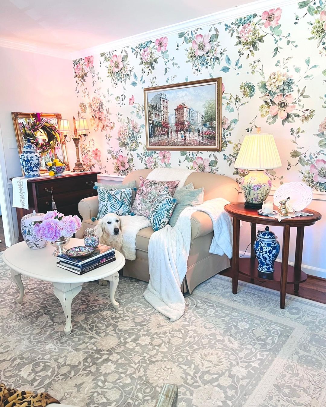 Gemütliches Wohnzimmer mit floraler Tapete, beigem Sofa und einem weißen Golden Retriever.