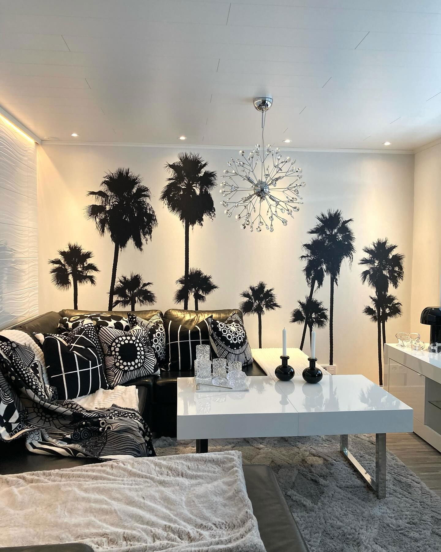 Living room with black and white decor, palm tree wall decals, and a crystal chandelier.