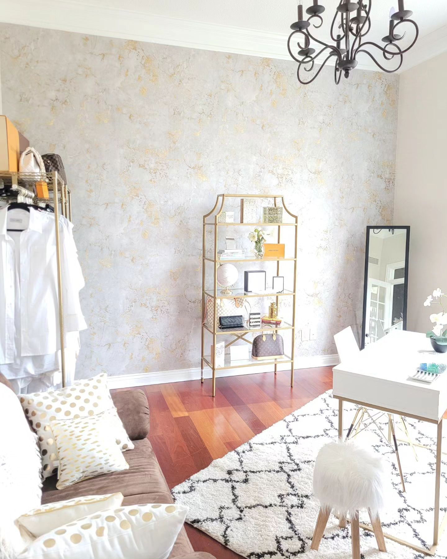 Interior with gold accents: clothing rack, shelving unit, desk, and patterned rug.
