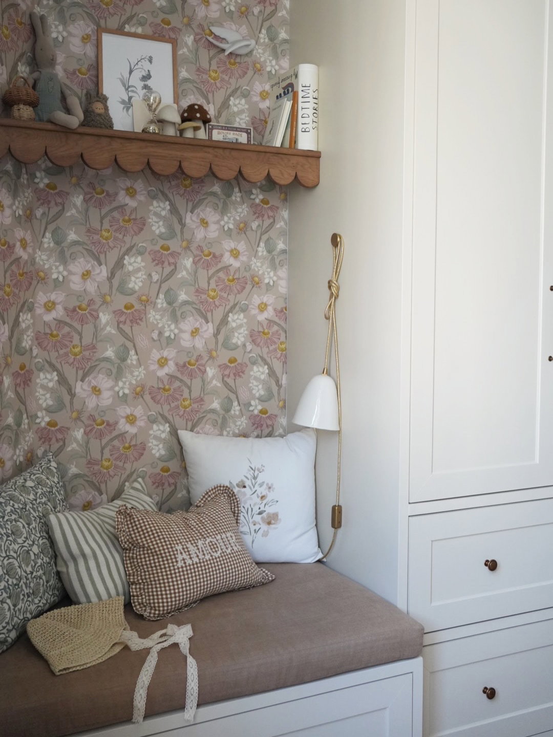 Cozy reading nook with floral wallpaper, plush pillows, and a white wall lamp.