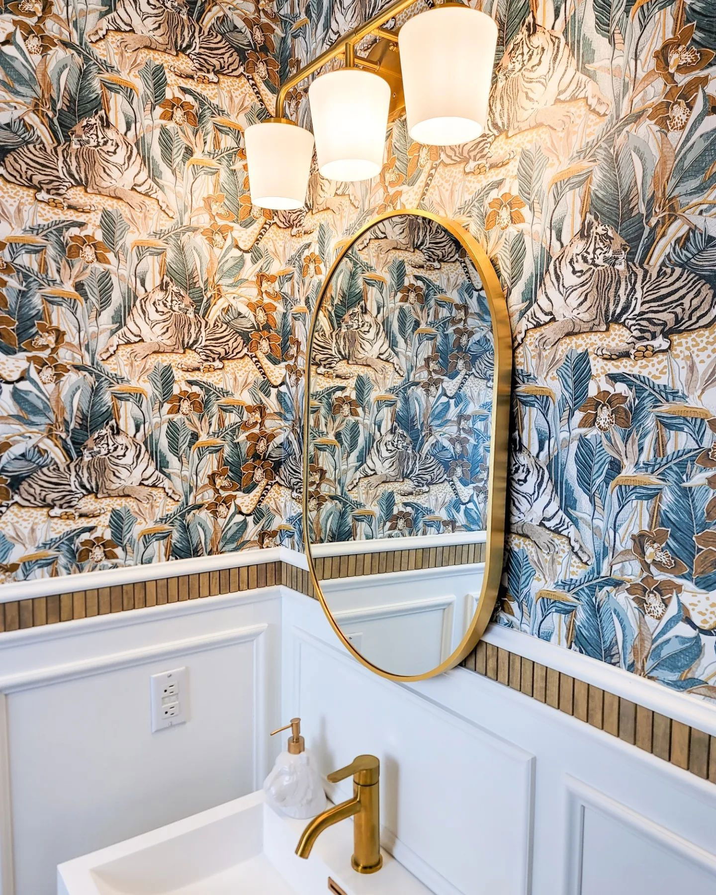 Badezimmer mit Tiger-Tapete, goldenem Spiegel und Wasserhahn, weißem Waschbecken und Wandvertäfelung.