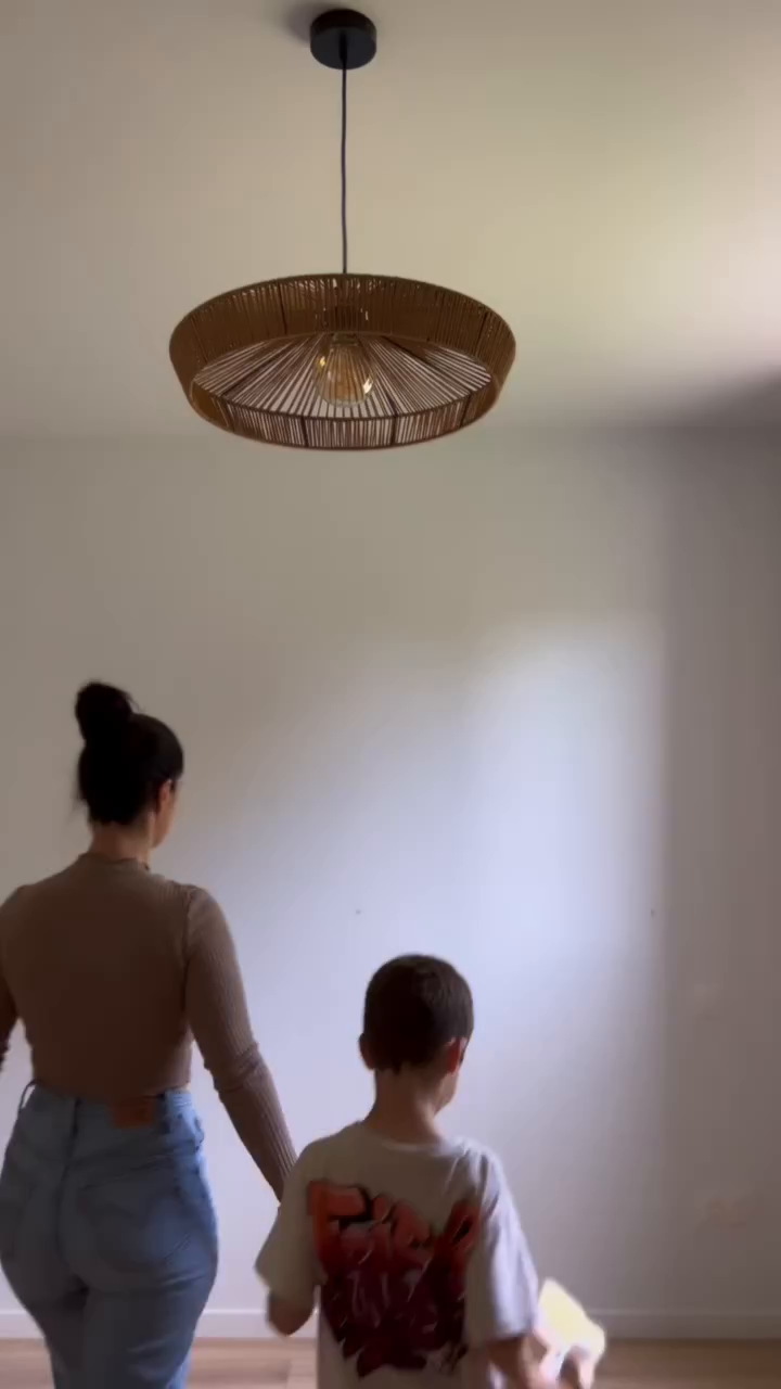 Woman and child holding hands, walking under a woven pendant light.