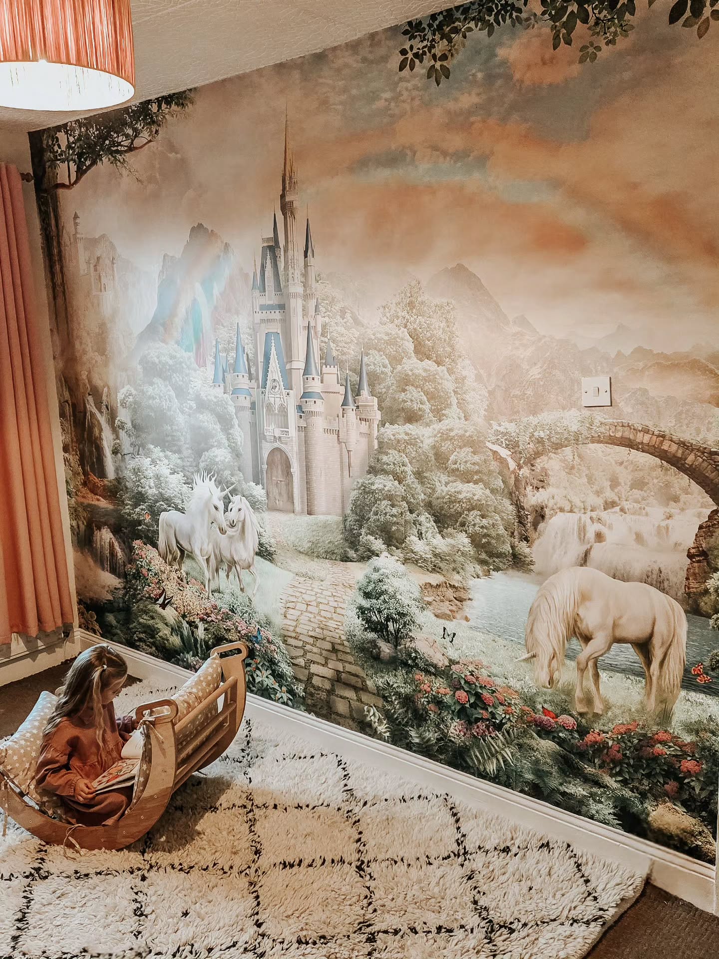 Child reading in a wooden rocker chair against a fantasy castle and unicorn wall mural.
