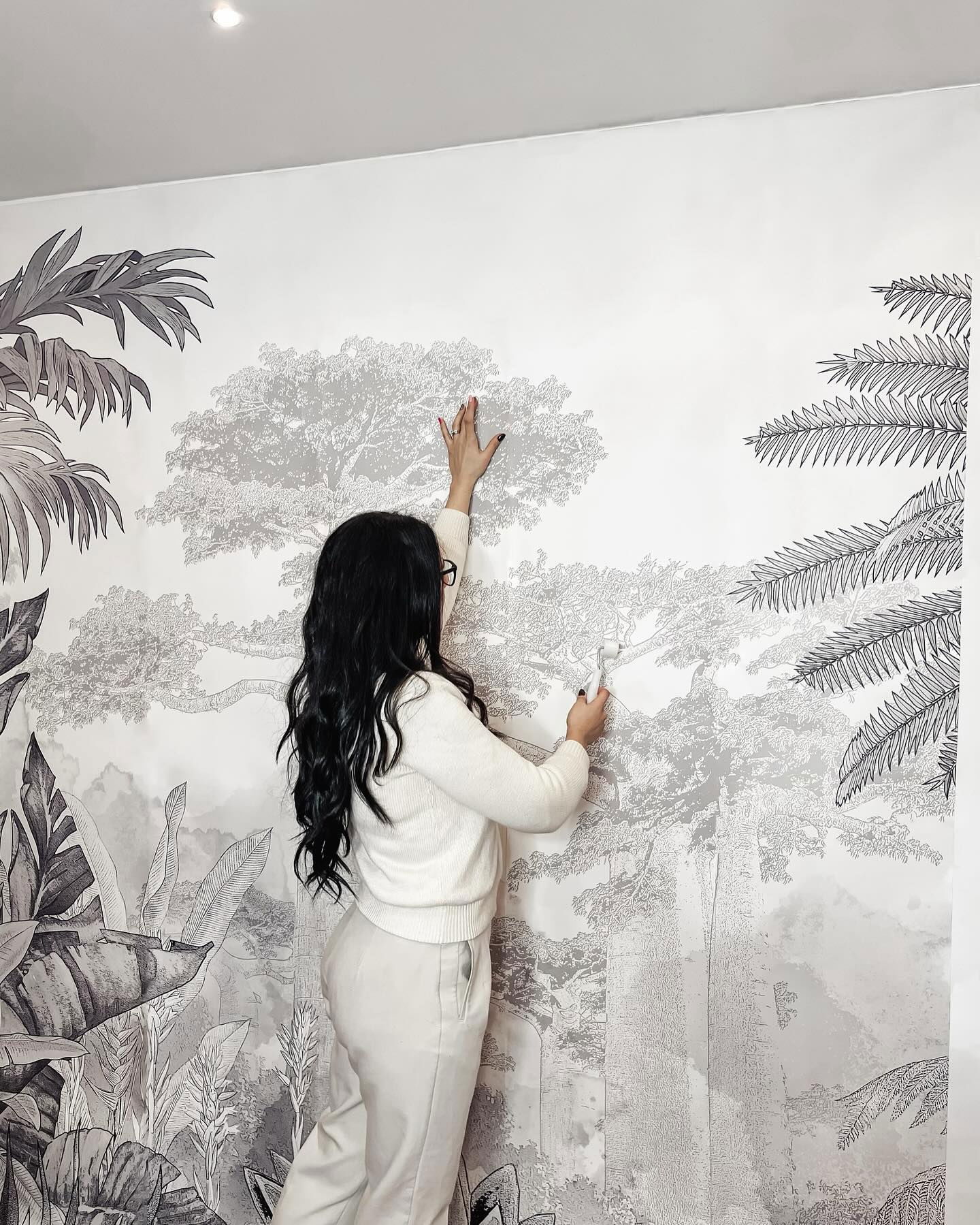 Kobieta wygładza czarno-biały tropikalny mural na ścianie.