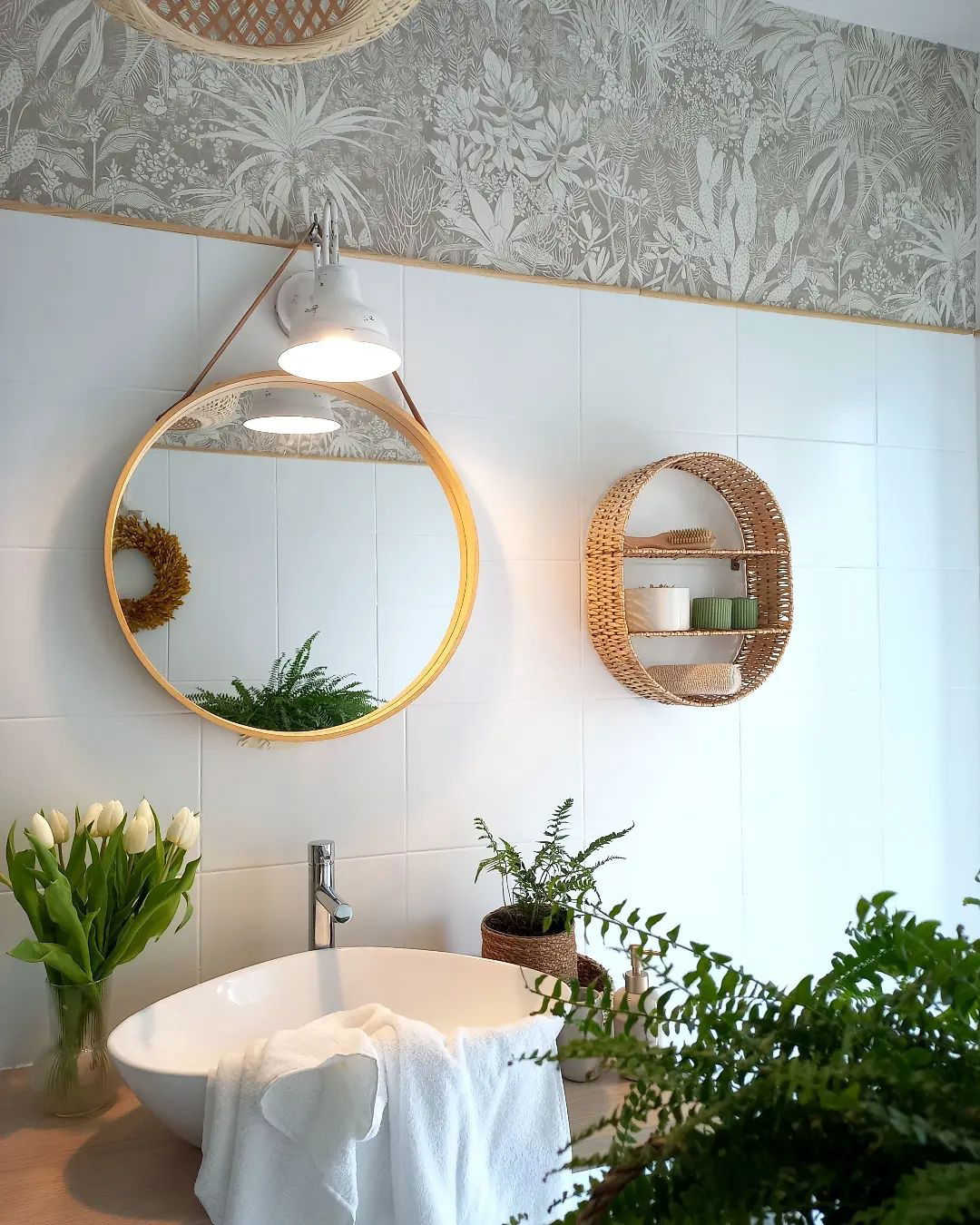 Bathroom interior with white vessel sink, round mirror, and botanical wallpaper.