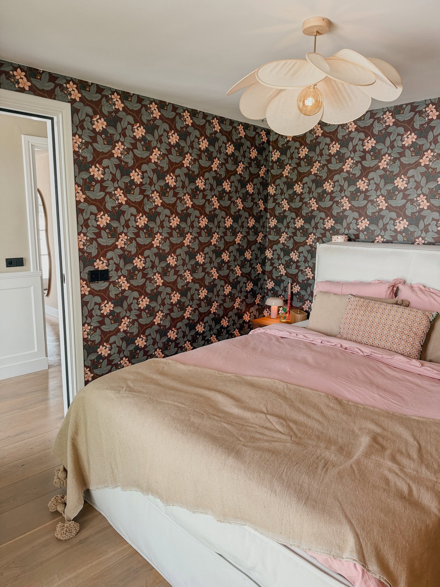 Soveværelse med blomstret tapet, pink sengetøj og en blomsterformet lampe.