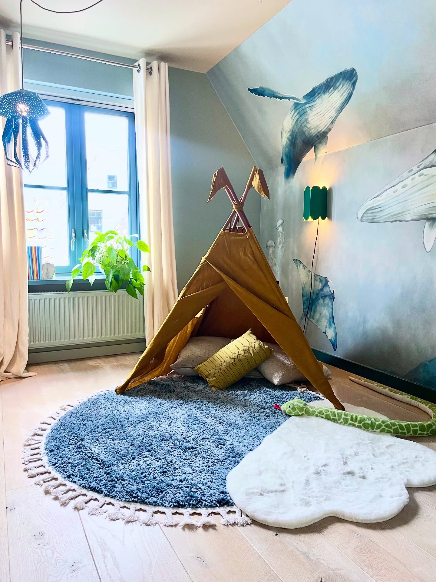 Child's room with a mustard-colored teepee, blue rug, and a wall with a whale mural.