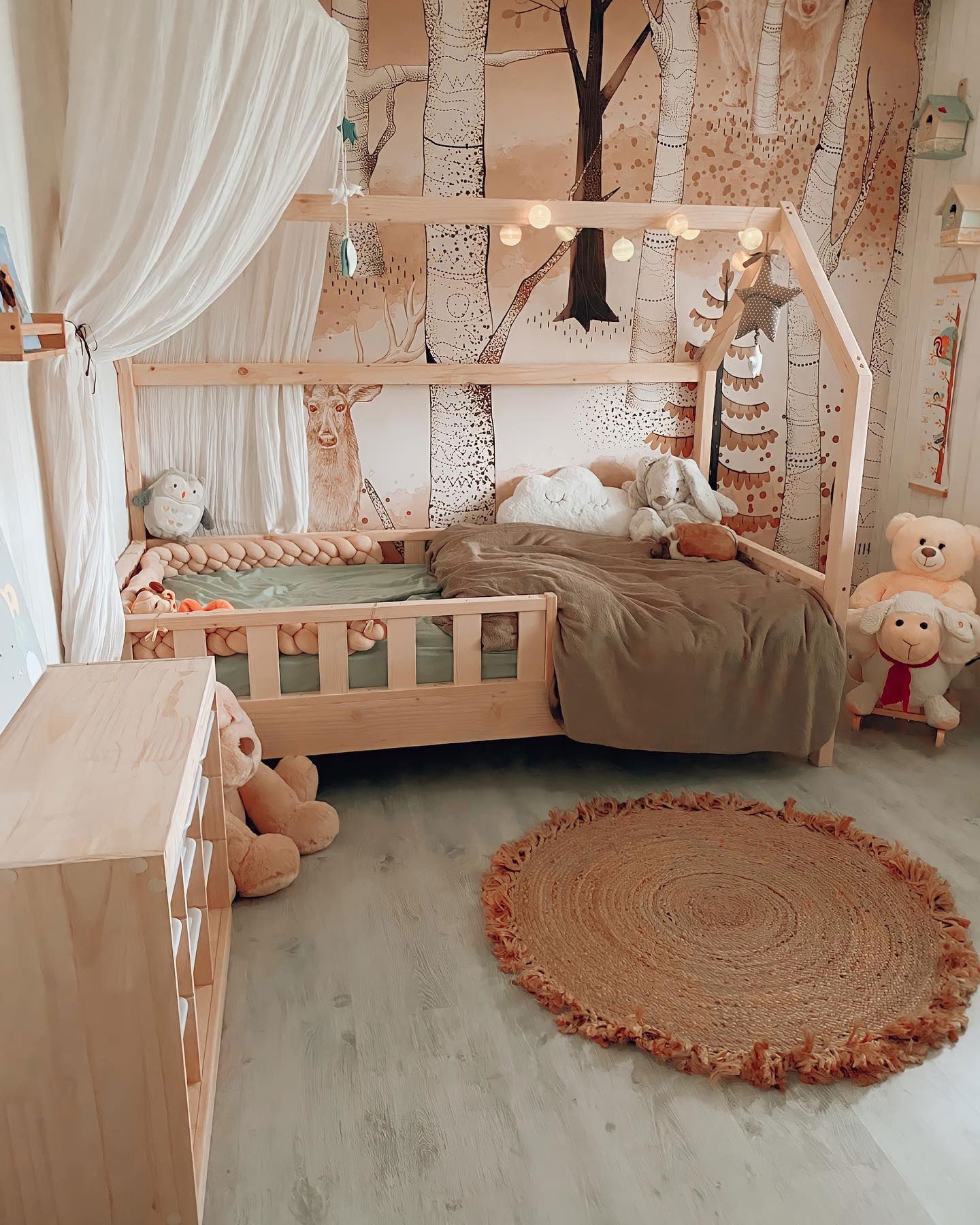 Kinderzimmer mit Holzbett in Hausrahmenform, Waldtapete und rundem Jute-Teppich.