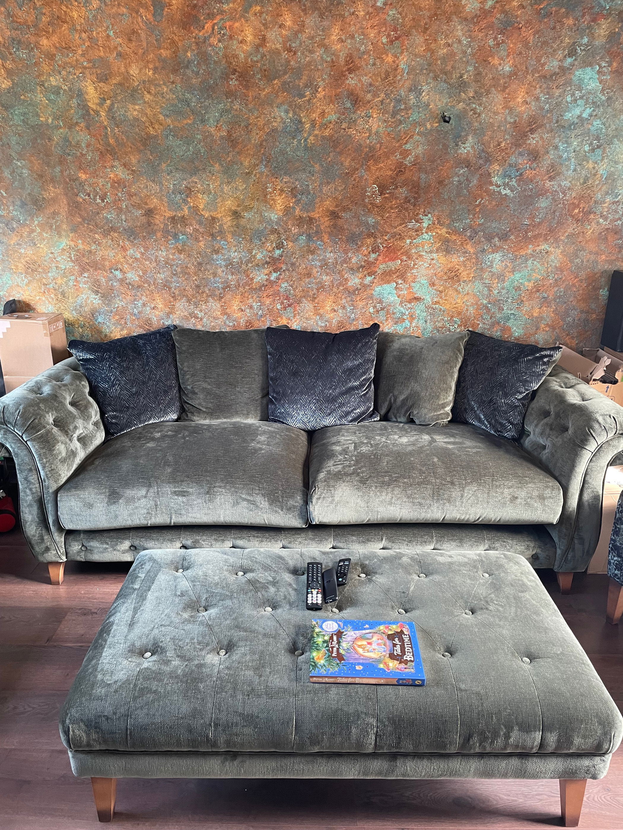 Green velvet sofa and matching tufted ottoman with books and remotes.