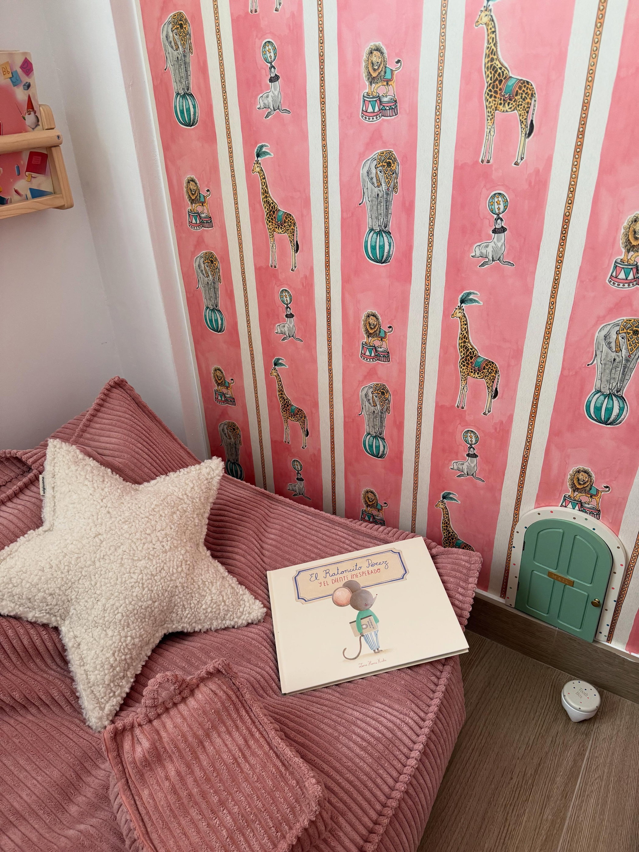 Pink corduroy beanbag chair with star pillow and children's book, next to circus animal wallpaper.