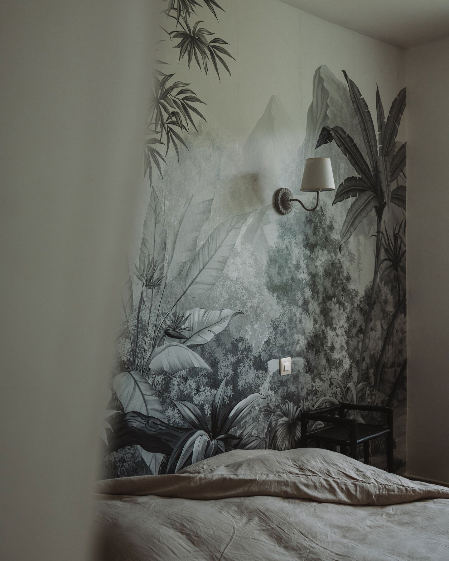 Soverom med tropisk veggmaleri, vegglampe og seng.