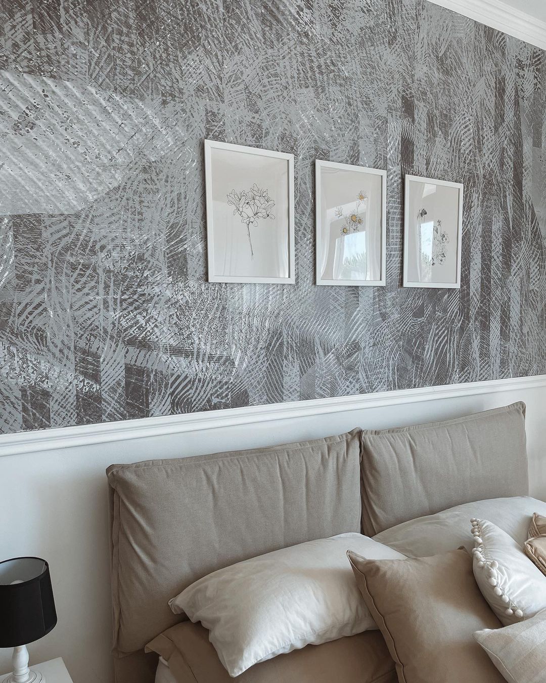 Schlafzimmer mit grauer gemusterter Tapete, weiß gerahmter Blumenkunst und einem Bett mit neutralen Kissen.