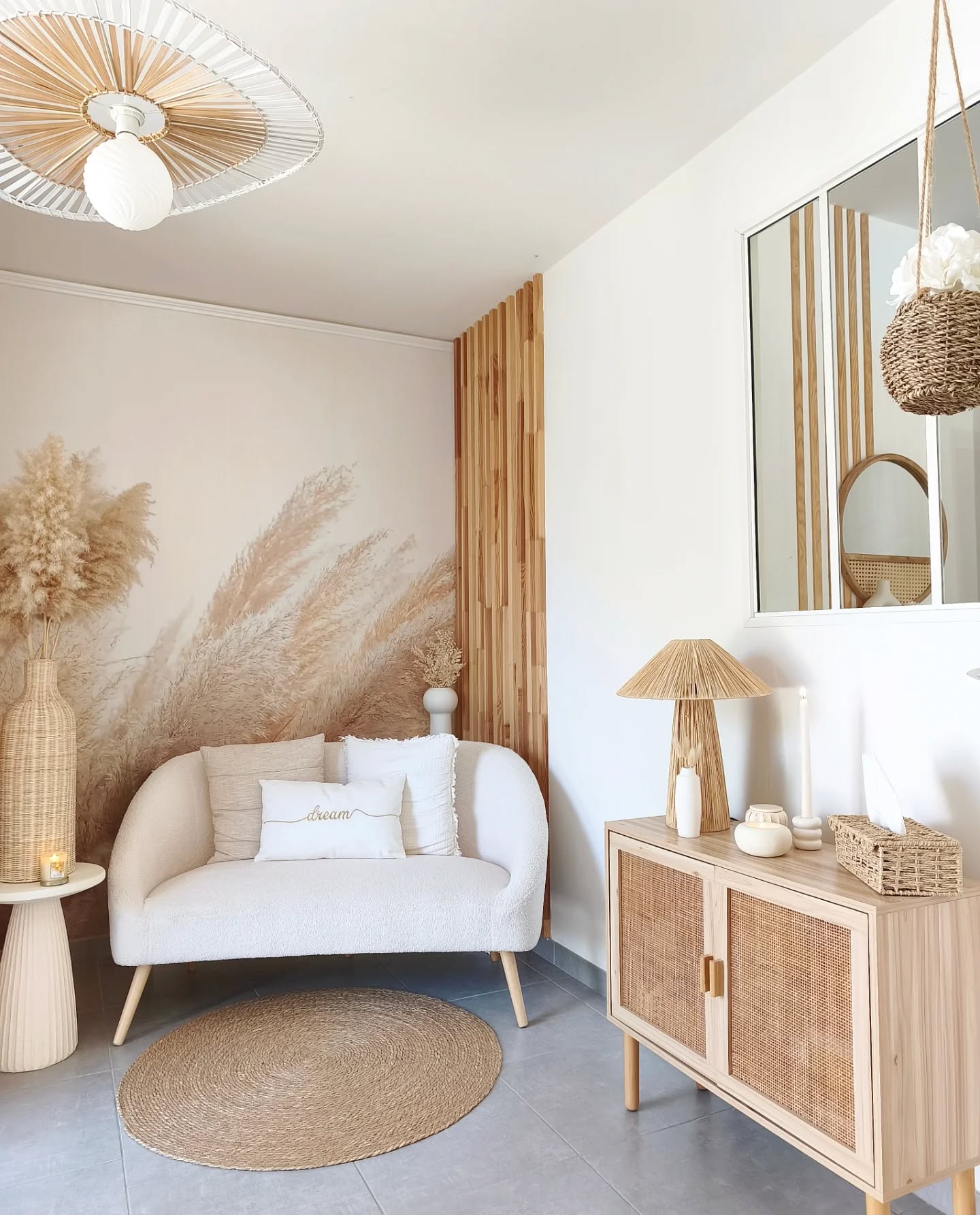 Una habitación luminosa con un sofá color crema, una alfombra redonda de yute y papel tapiz de hierba de la pampa. Un mueble de madera clara con puertas de ratán exhibe decoración tejida.