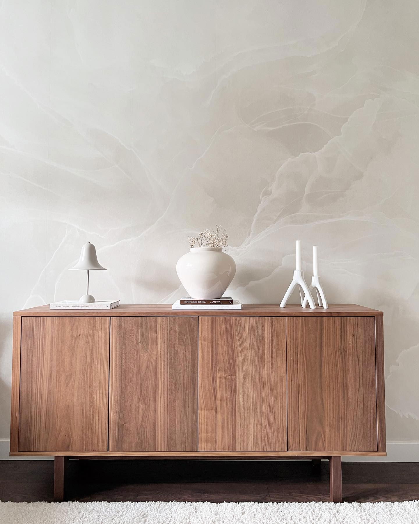 Credenza in noce con vaso bianco, lampada e portacandele su carta da parati in marmo.