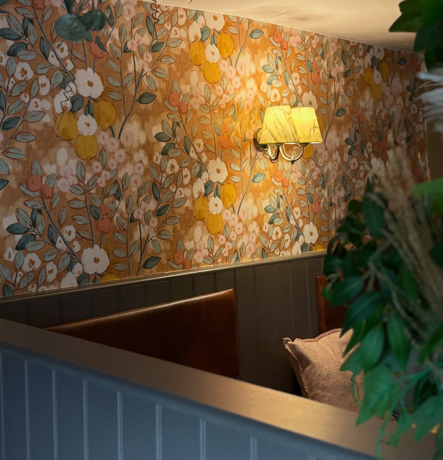 A wall with a floral wallpaper featuring lemons and white flowers, with a brass sconce light fixture.
