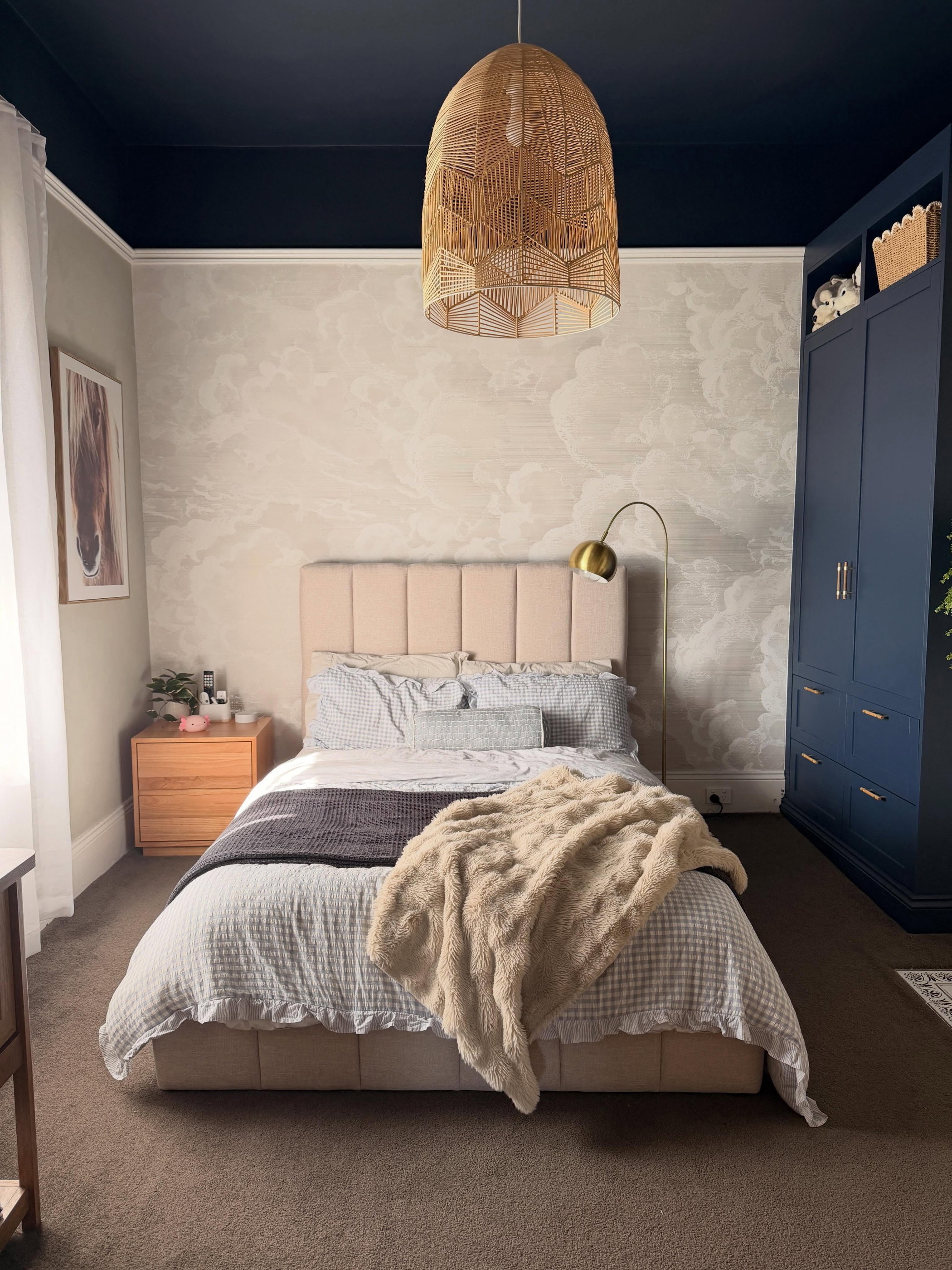 Bedroom with queen bed, cloud wallpaper, navy wardrobe, and woven pendant light.