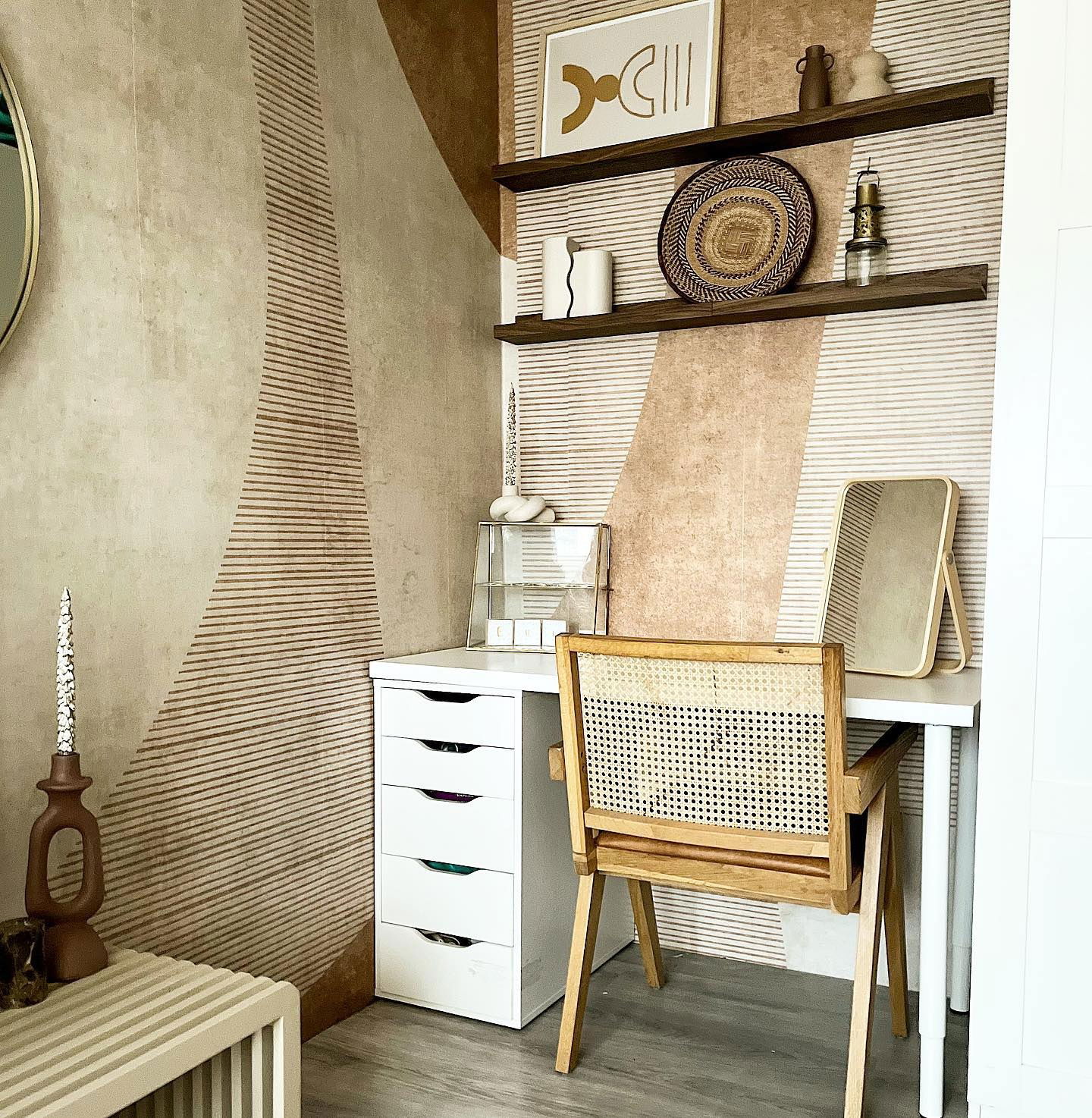 Interieur met wit bureau, lades en een stoel met rieten rug tegen een behang met patroon. Op de planken staan kunst en decoratie.