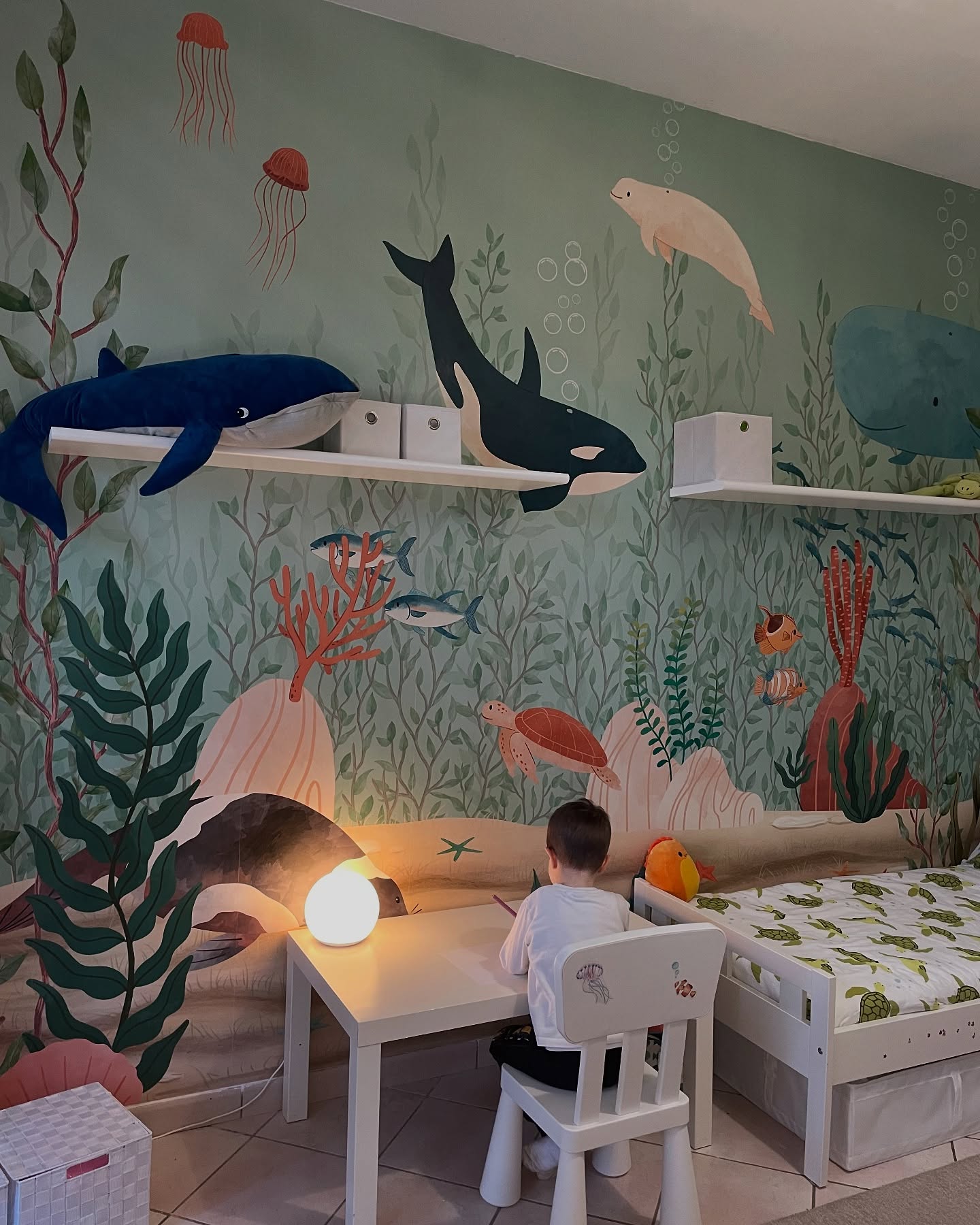 Child sits at a table in a sea-themed room with ocean mural.