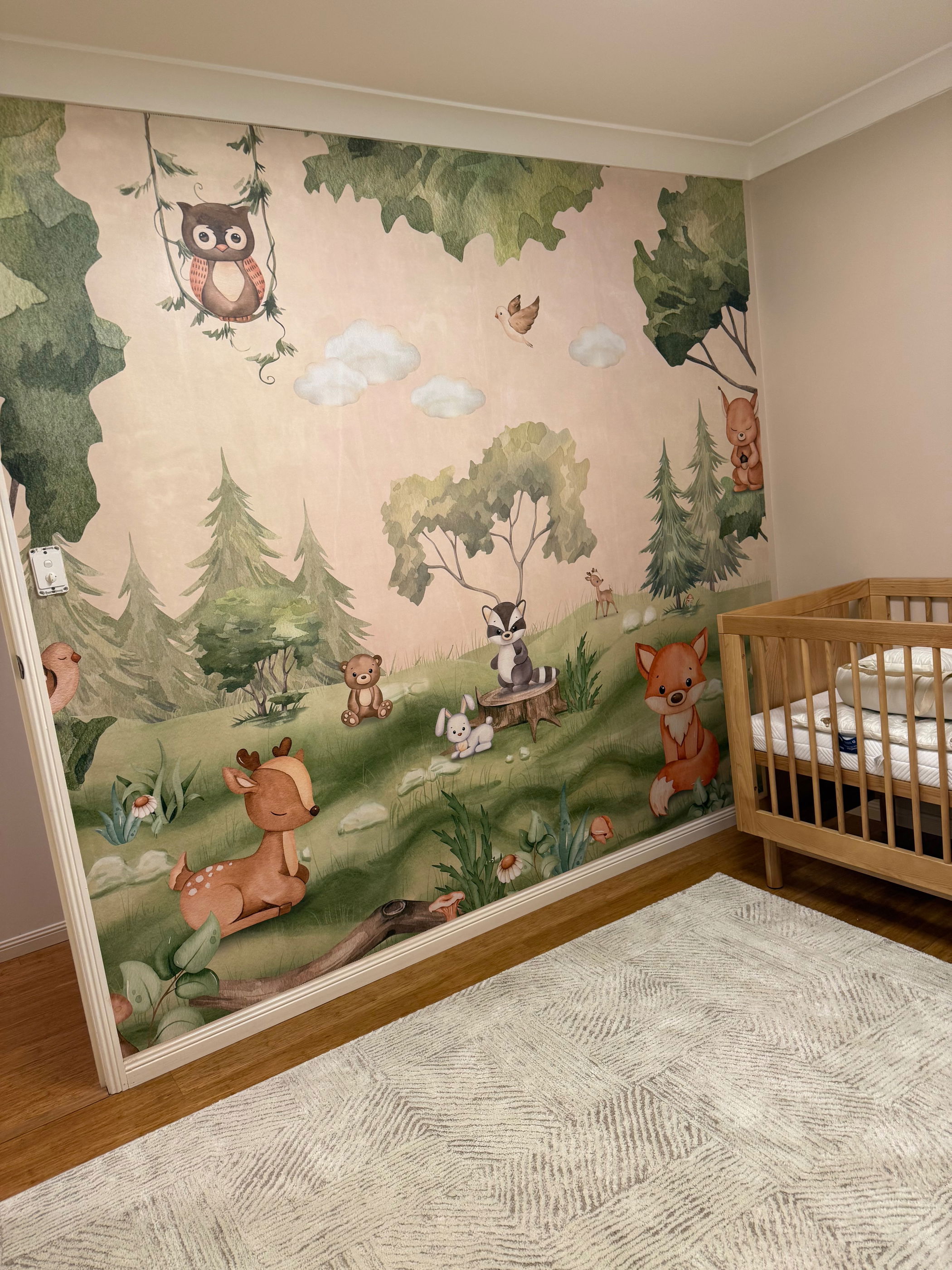 Nursery with woodland animal wallpaper and wooden crib.