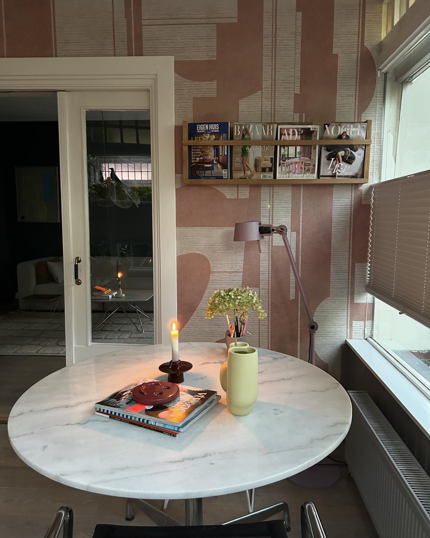 Interieur met ronde marmeren tafel, boeken, kaars en gele vaas. Tijdschriftenrek op behang met patroon.