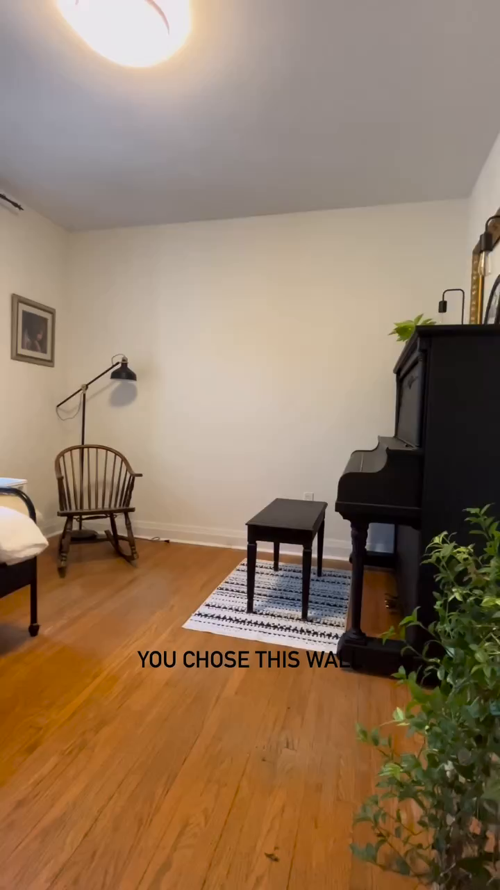 Cozy room with black upright piano, stool on striped rug, and wooden rocking chair.
