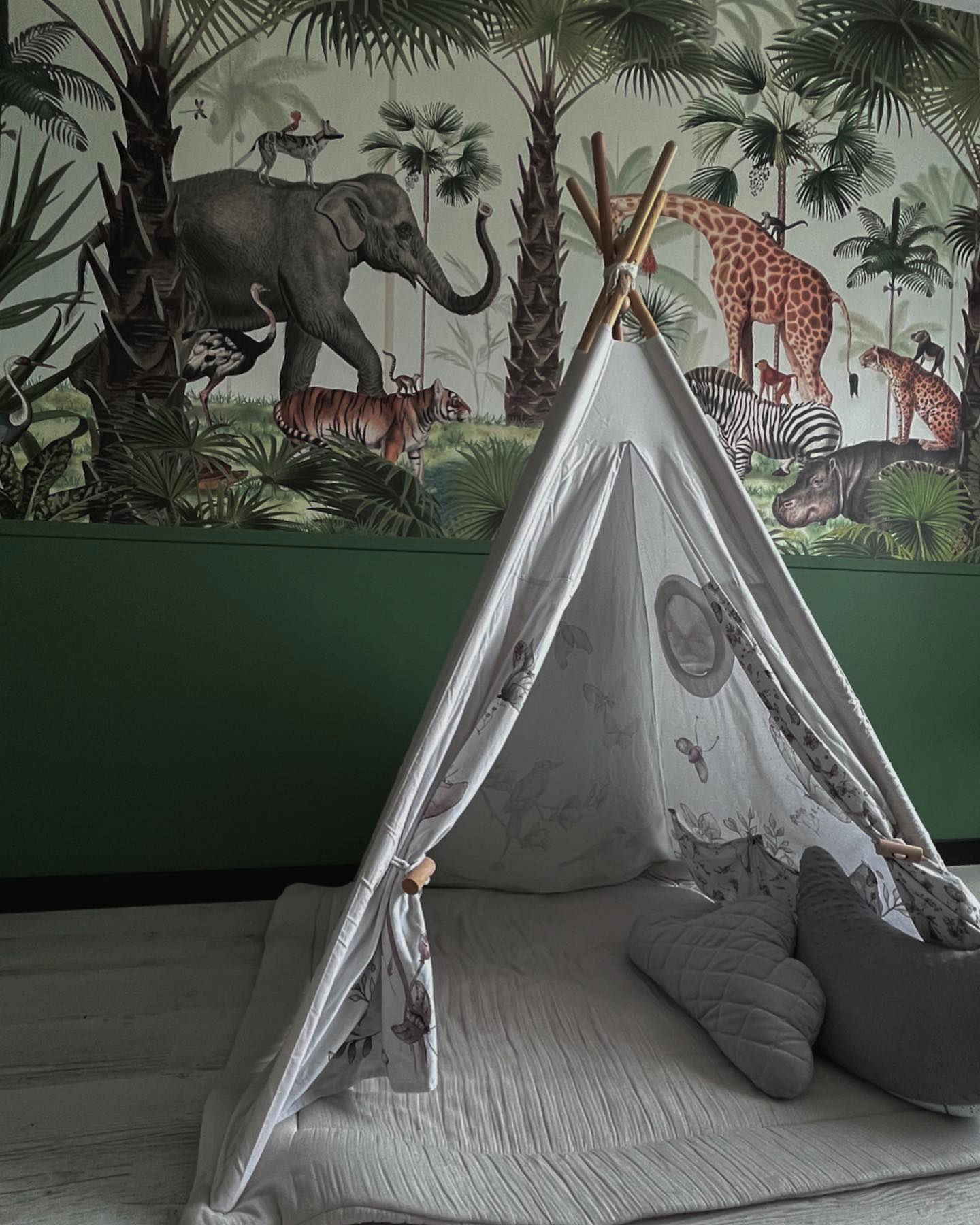 Barne-teepee med puter på en matte, satt mot en jungel-tapet.