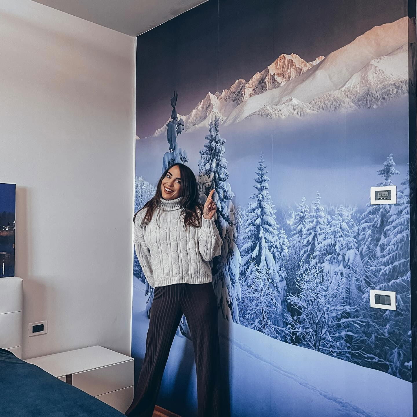 A woman poses in front of a winter mountain scene mural.