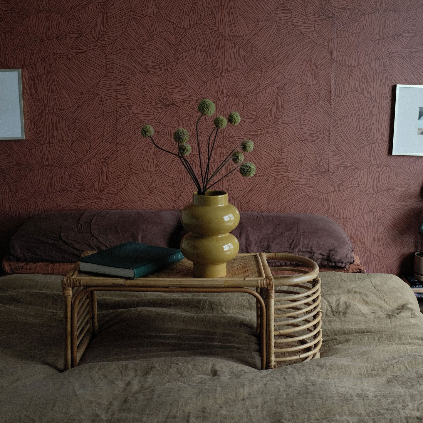 Bedroom scene with a rattan bed tray holding a vase of flowers and book.