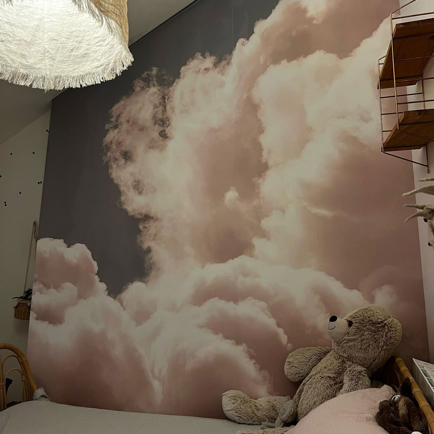Child's bedroom with cloud wallpaper, teddy bear on bed, and fringed light fixture.