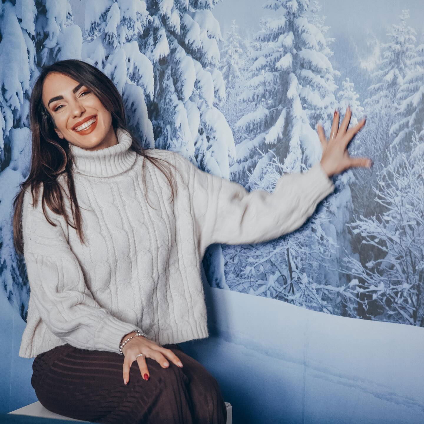 A smiling woman in a white turtleneck sweater poses in front of a wintery backdrop.
